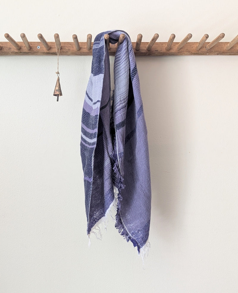 Purple and white scarf hanging on a wooden rack against a white wall.