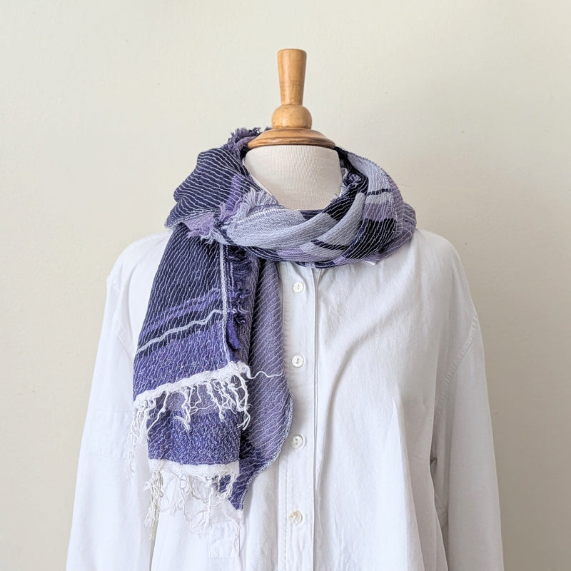 Mannequin wearing a white shirt with a purple scarf draped over it against a plain background