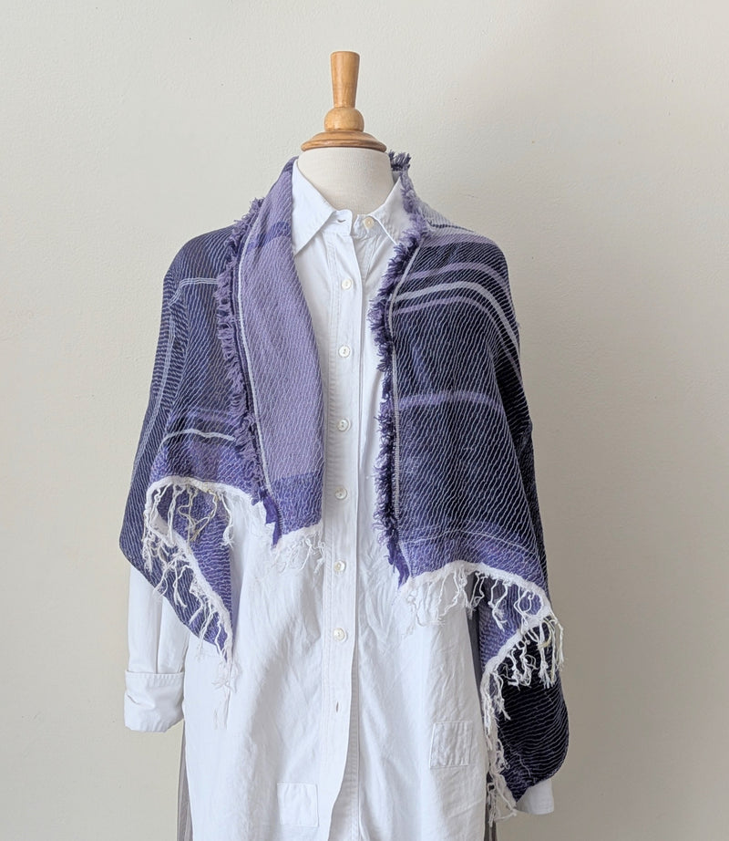 Mannequin wearing a white shirt with a purple shawl draped over it on a plain background