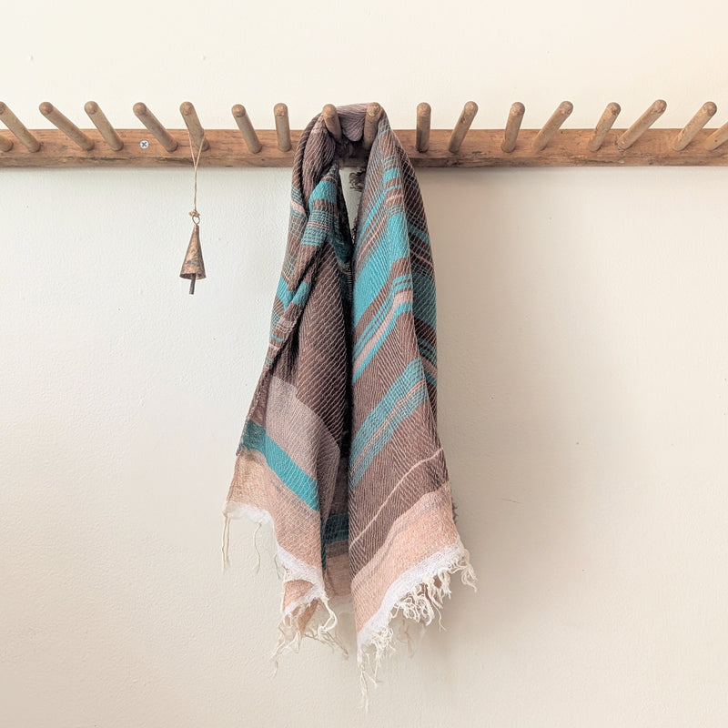 Striped brown and turquoise hanging on a wooden rack against a white wall