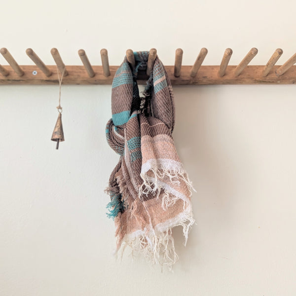 Brown and teal scarf hanging on a wooden rack against a white wall.