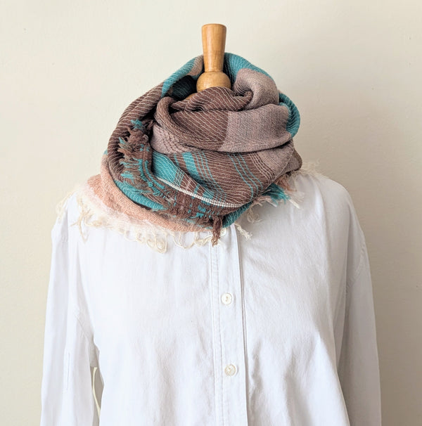 Brown and teal scarf draped over a white shirt on a mannequin against a plain background
