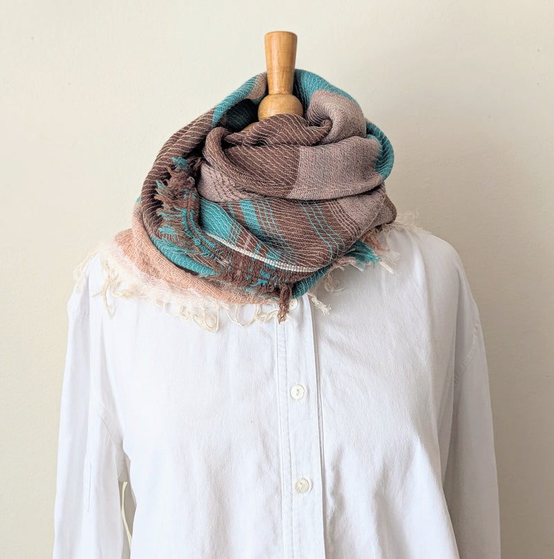 Brown and teal scarf draped over a white shirt on a mannequin against a plain background