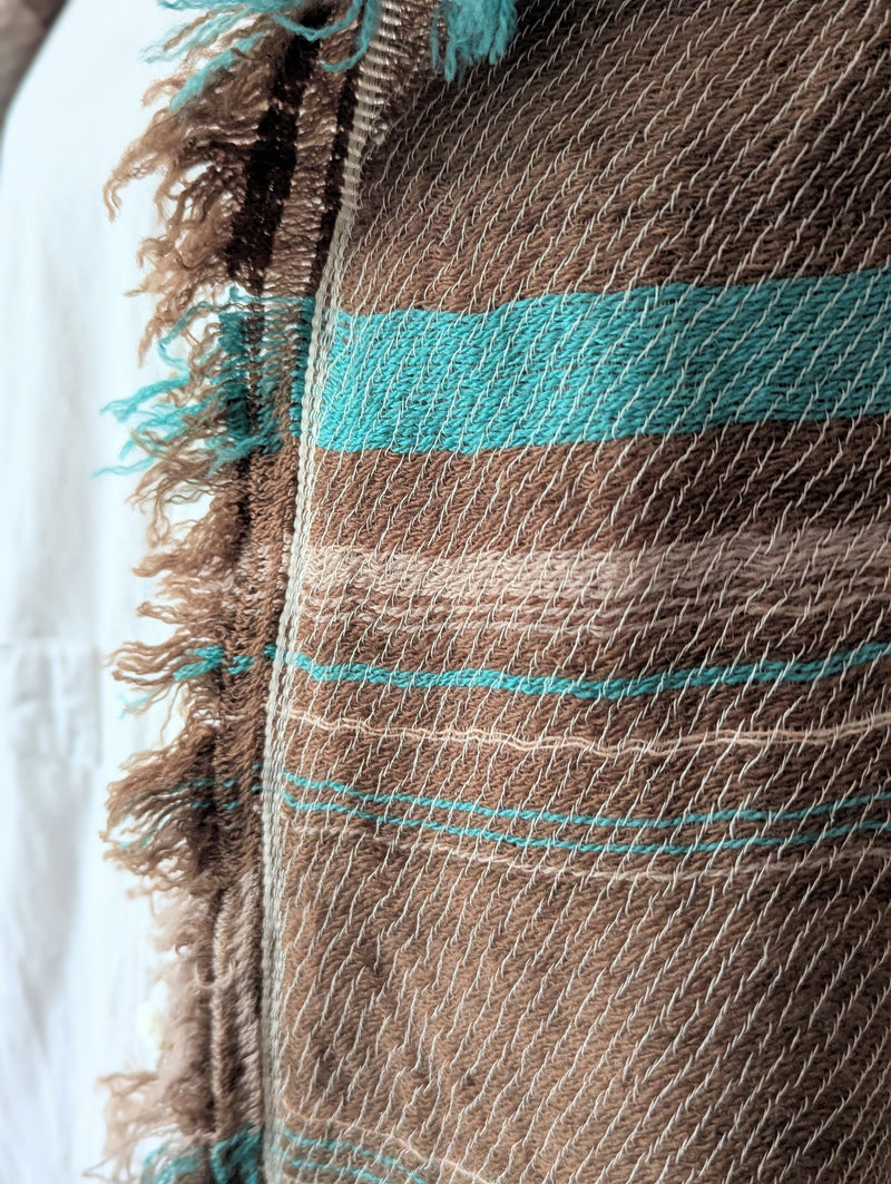 Close-up of a brown scarf with turquoise stripes and frayed edges.