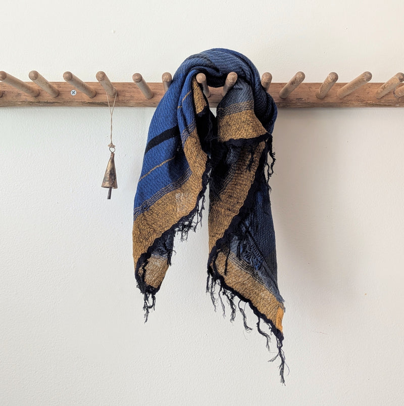 Blue and brown striped scarf hanging on a wooden rod against a white wall.