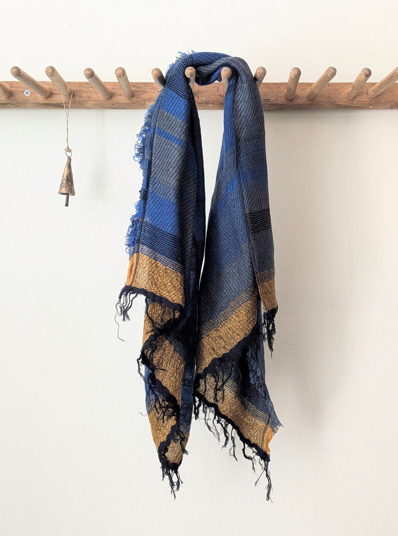 Blue and brown striped scarf hanging on a wooden rod against a white wall.
