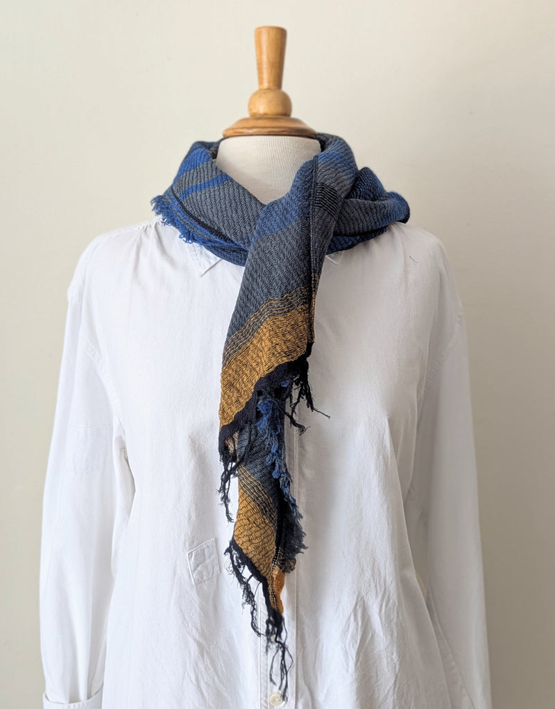 Blue and brown striped scarf hanging on a wooden rod against a white wall.