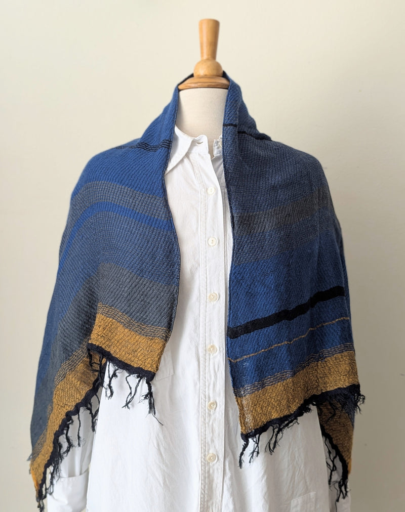Mannequin wearing a white shirt with a blue and gold striped shawl draped over it on a plain background