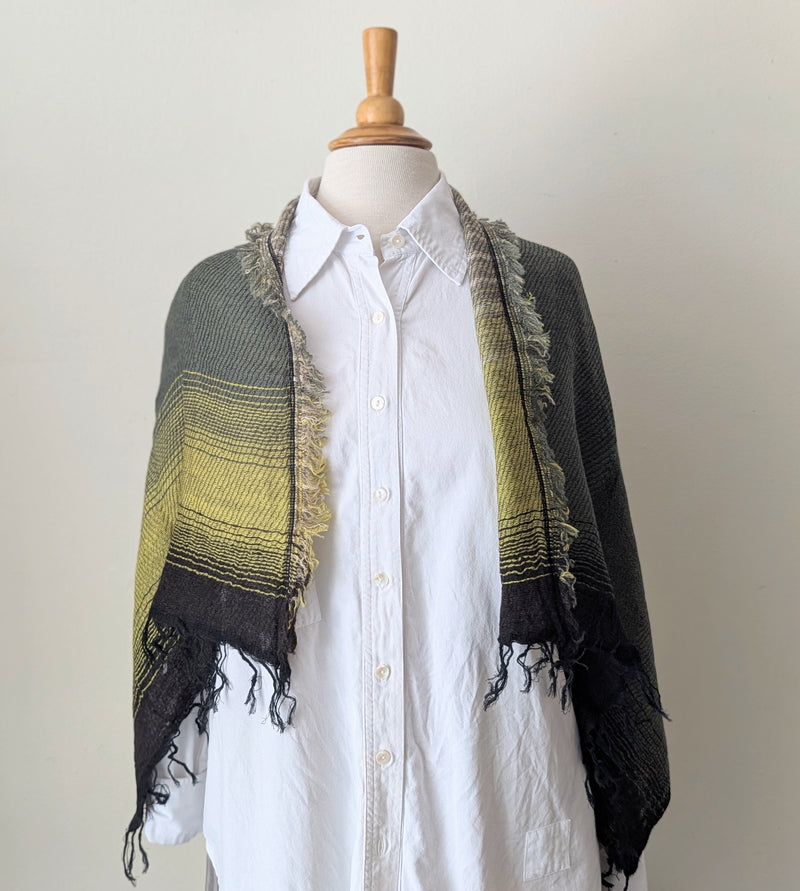 Mannequin wearing a white shirt with a green and black patterned shawl draped over it against a plain background.