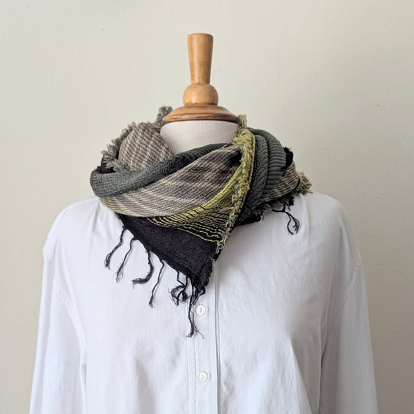 Mannequin wearing a green, brown and black scarf with a white shirt against a plain background