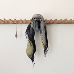 Scarf with green and black stripes hanging on a wooden rack against a white wall