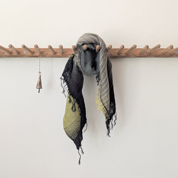 Scarf with green and black stripes hanging on a wooden rack against a white wall