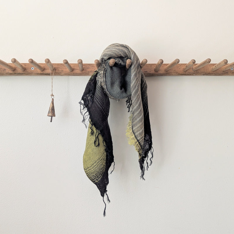 Scarf with green and black stripes hanging on a wooden rack against a white wall