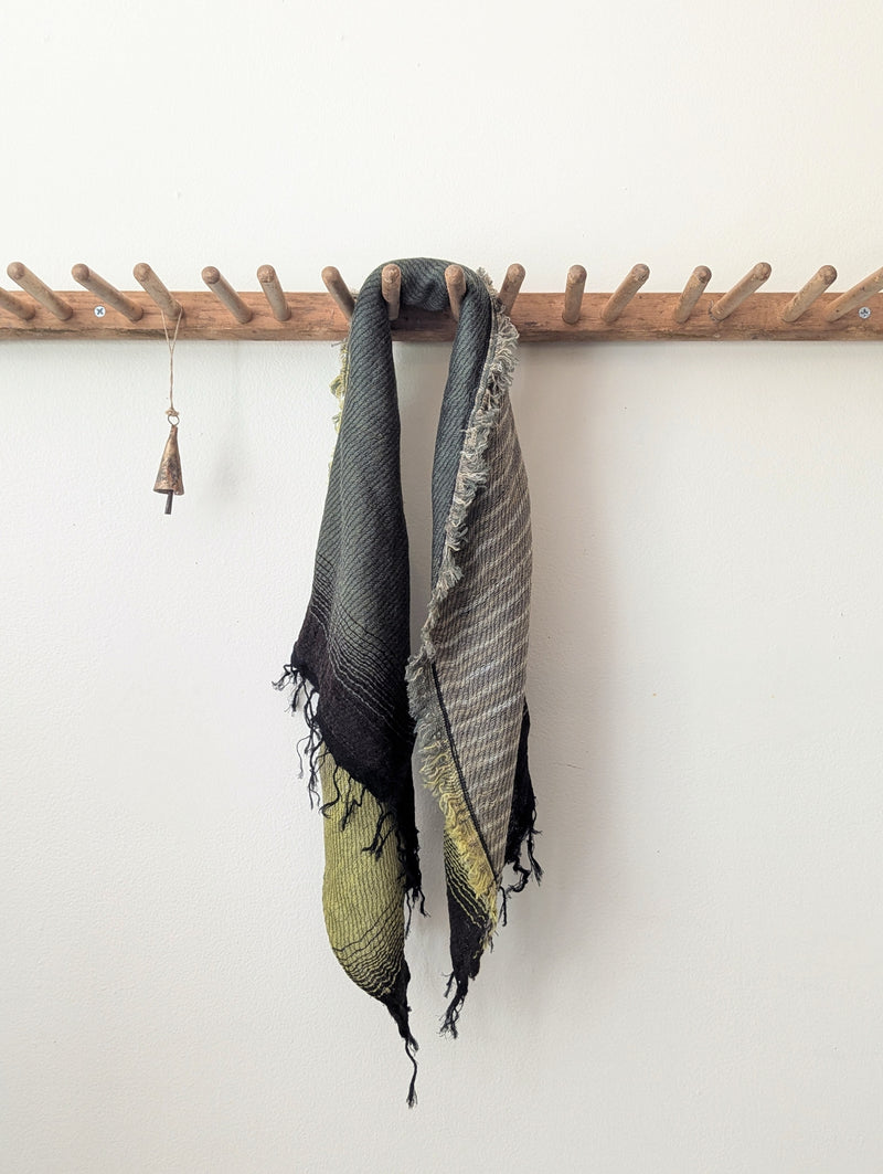 Scarf with green and black stripes hanging on a wooden rack against a white wall