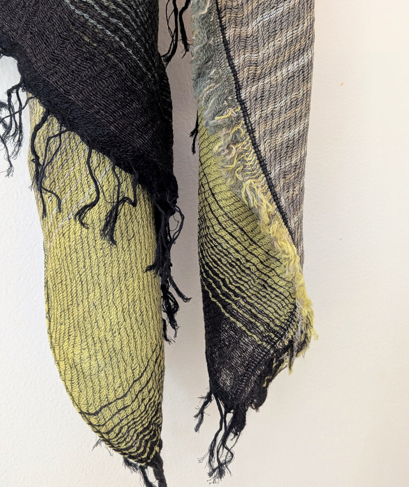 Scarf with yellow green and black stripes hanging against a white wall