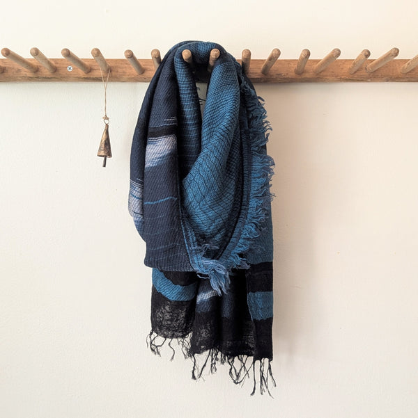 Blue and teal plaid scarf hanging on a wooden coat rack against a white wall.