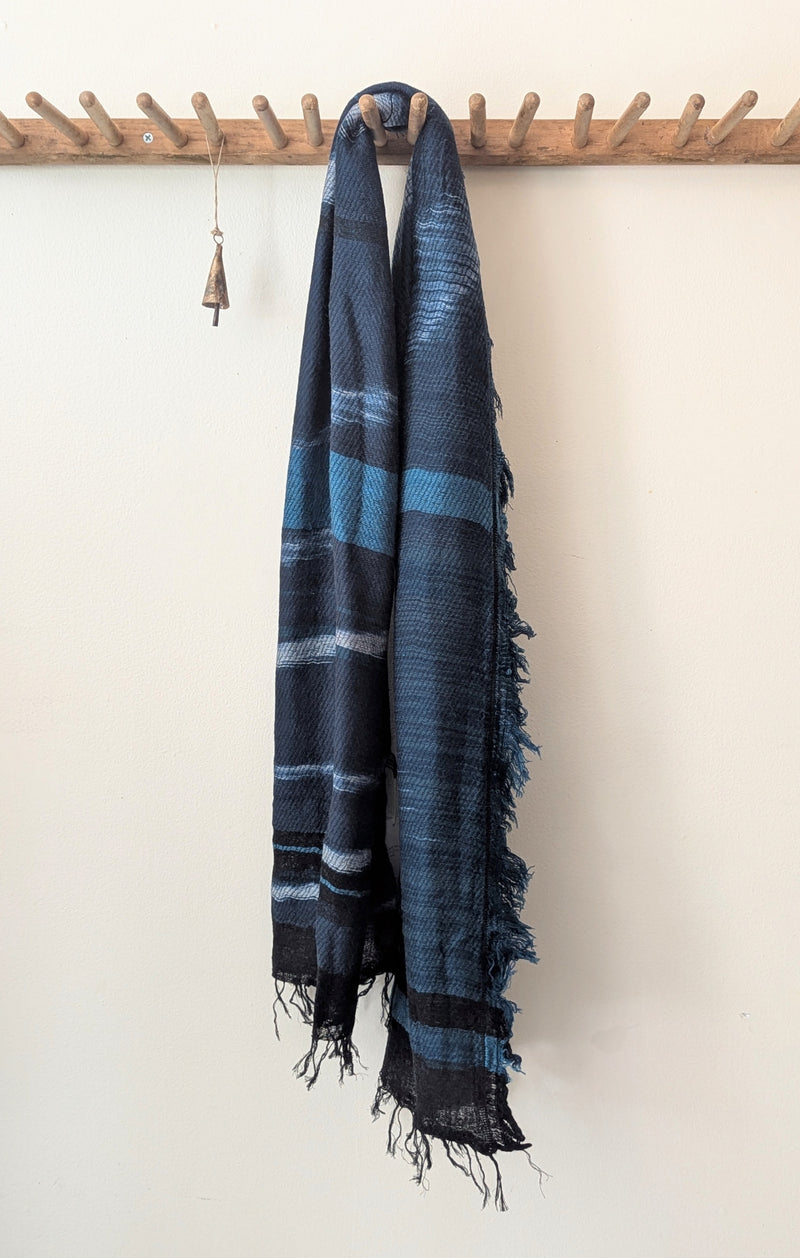 Blue and teal plaid scarf hanging on a wooden coat rack against a white wall.