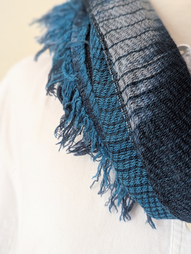 Blue and teal plaid scarf hanging on a wooden coat rack against a white wall.