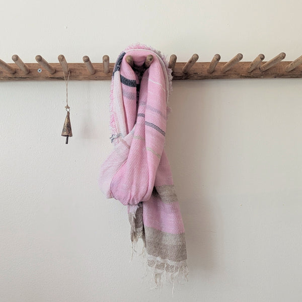 Pink scarf draped over a wooden coat rack against a white wall