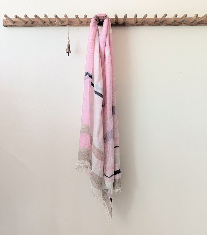Pink scarf draped over a wooden coat rack against a white wall
