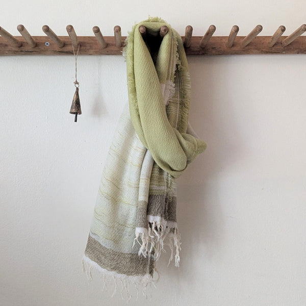 Pale green and beige striped scarf hanging on a wooden rack against a white wall.