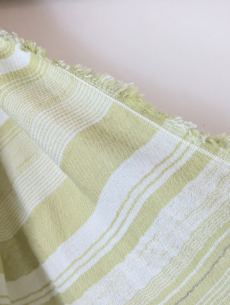 Pale green and beige striped scarf hanging against a white wall.