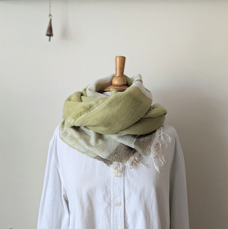 Pale green and beige striped scarf draped over a white shirt on a mannequin against a plain background