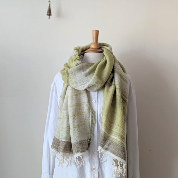 Pale green and beige striped scarf draped over a white shirt on a mannequin against a plain background