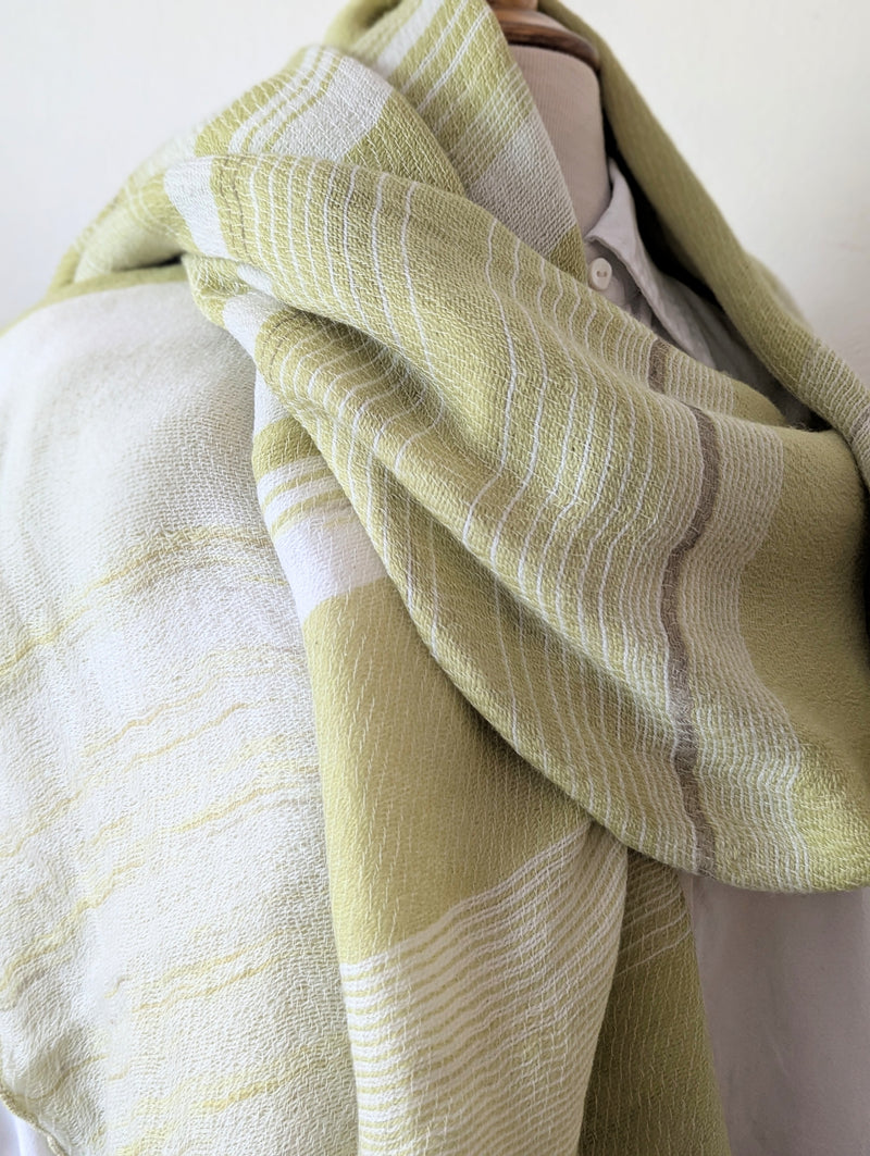 Pale green and beige striped scarf draped over a white shirt on a mannequin against a plain background