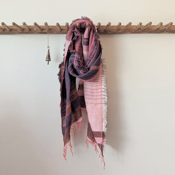 Rose pink and blue plaid scarf draped over a wooden rack against a white wall