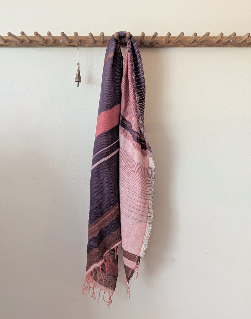 Rose pink and blue plaid scarf draped over a wooden rack against a white wall
