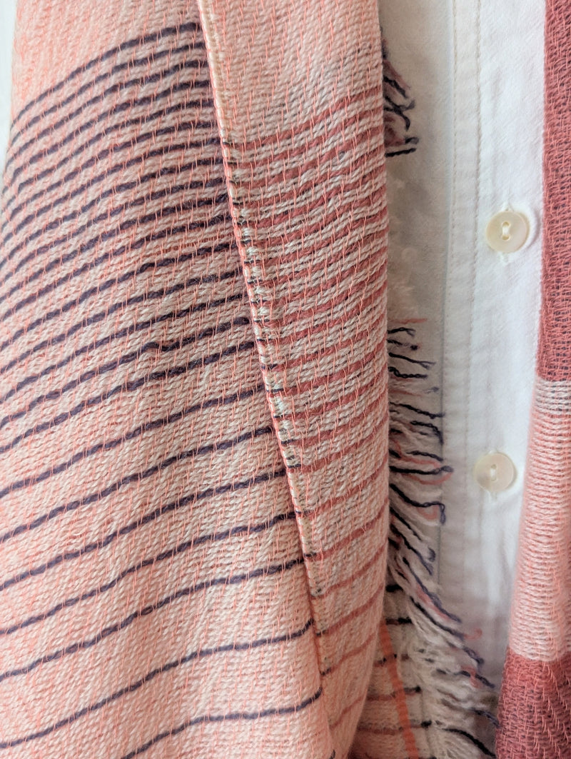 Rose pink and blue plaid scarf draped over a wooden rack against a white wall