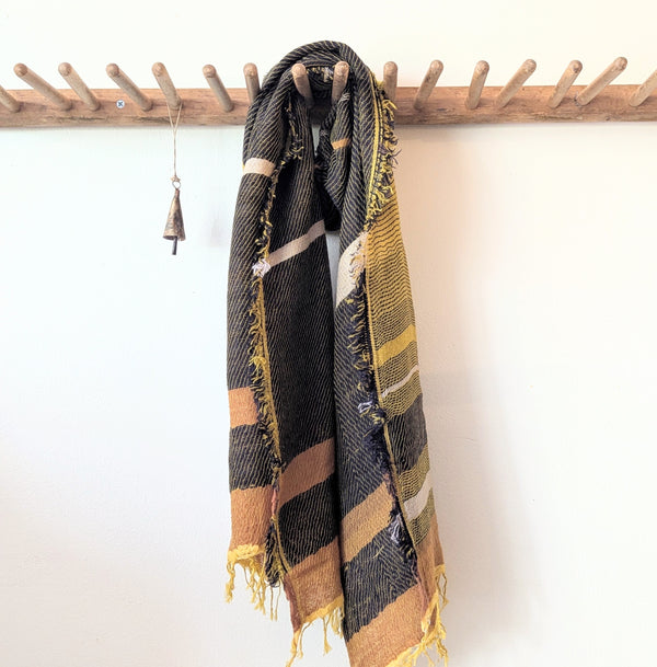 Plaid scarf with yellow and brown tones draped over a wooden rack against a white background