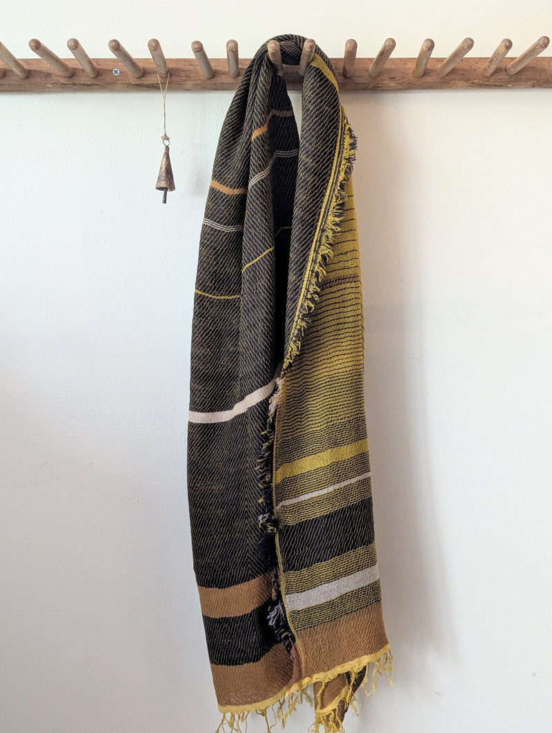 Striped ochre and black scarf hanging on a wooden rack against a white wall