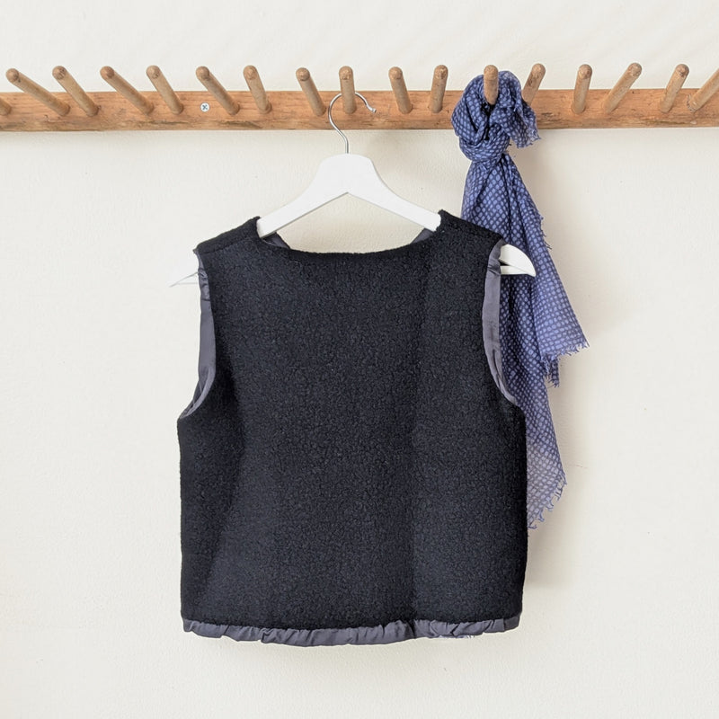 Back of a black wool vest on a hanger with a wooden rack in the background