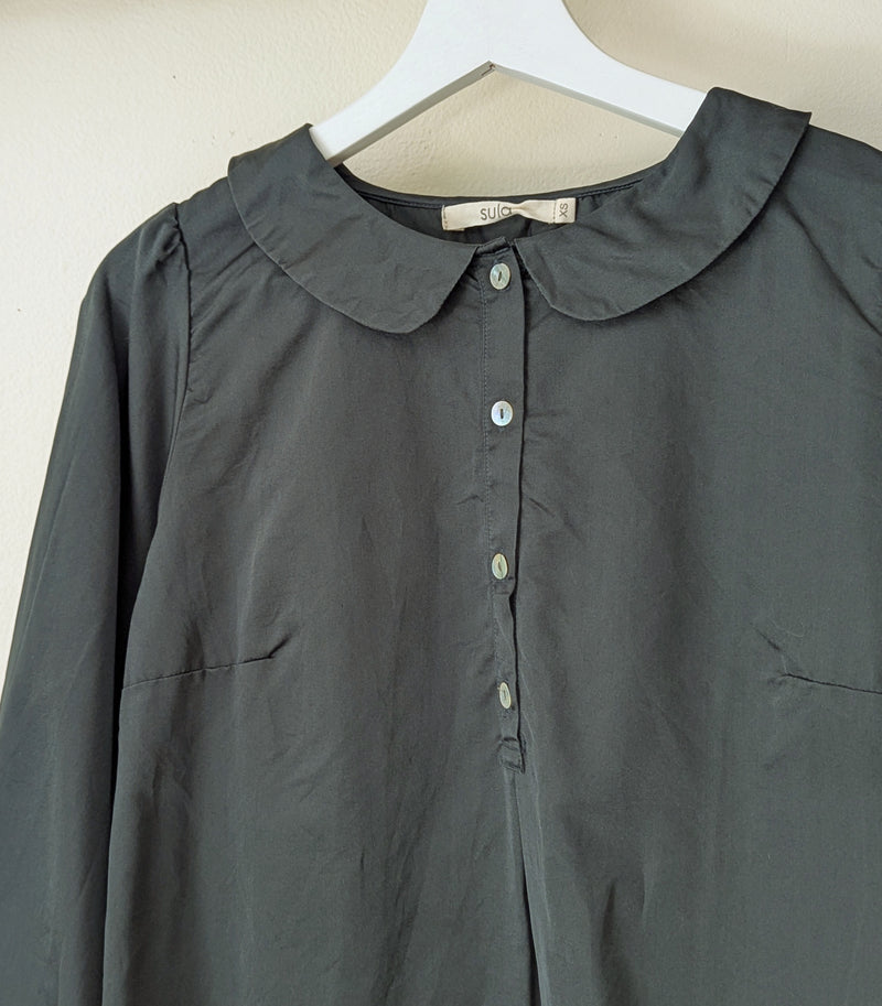 Dark green blouse with a collar on a hanger against a beige background