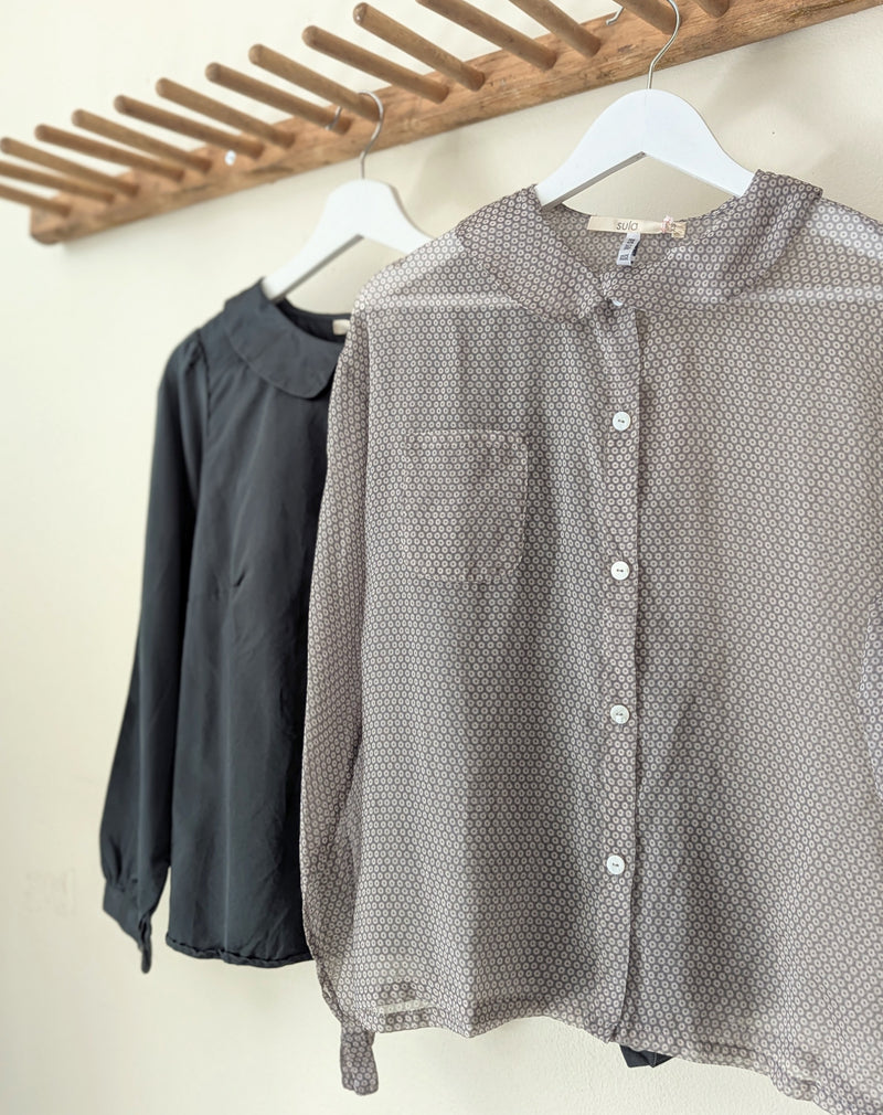 Two shirts hanging on a rack, one dark green and one  sheer patterned gray, against a neutral background.