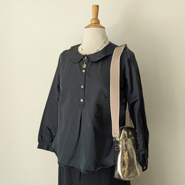 Dark green colored blouse on a mannequin with a beige strap and small bag against a plain background