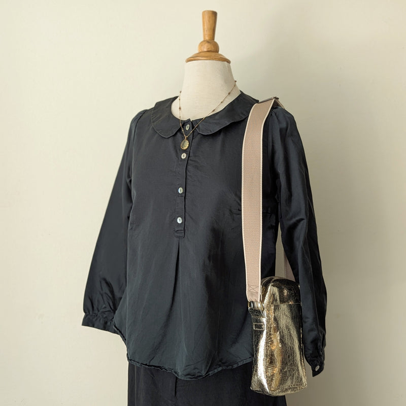 Dark green colored blouse on a mannequin with a beige strap and small bag against a plain background
