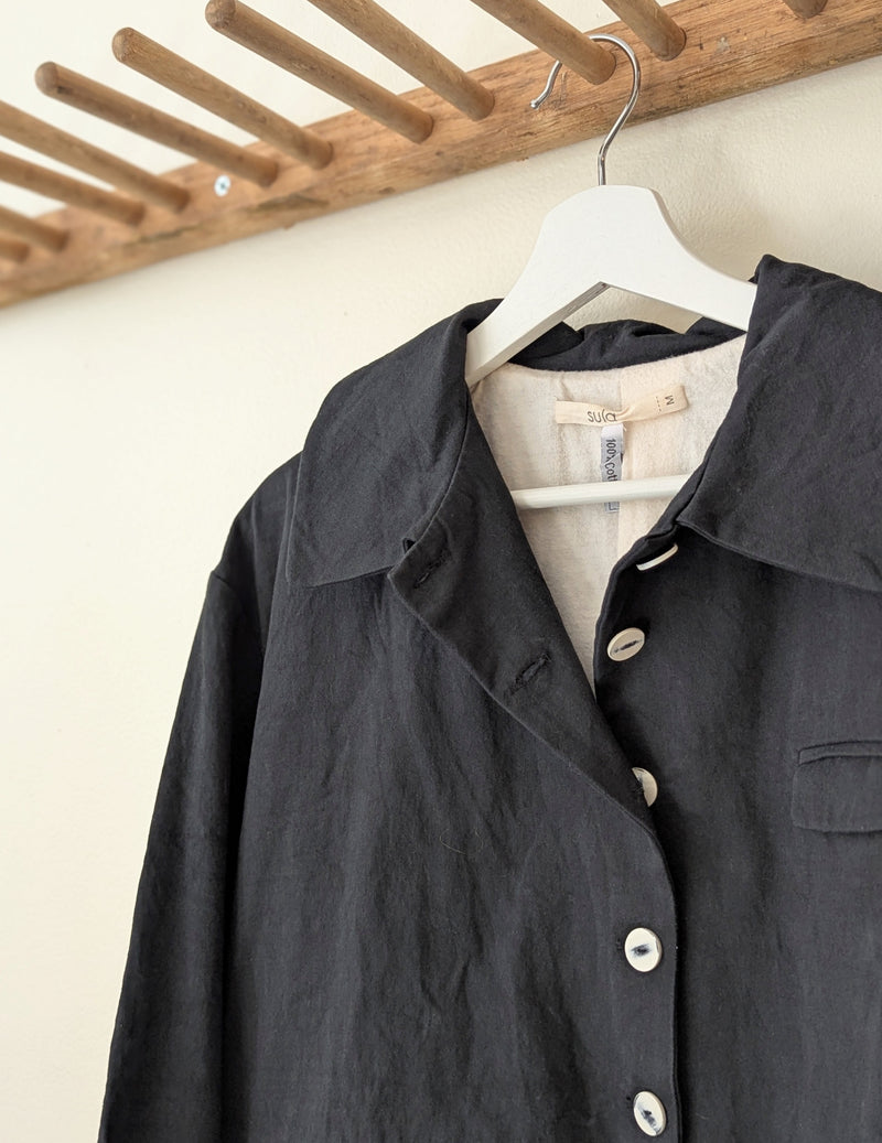Dark coat with buttons on a hanger against a wooden rack background