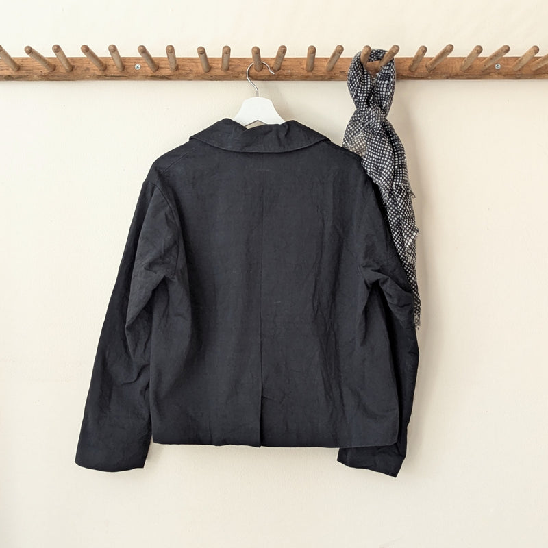 Black jacket on a hanger against a white wall with a wooden rack above.