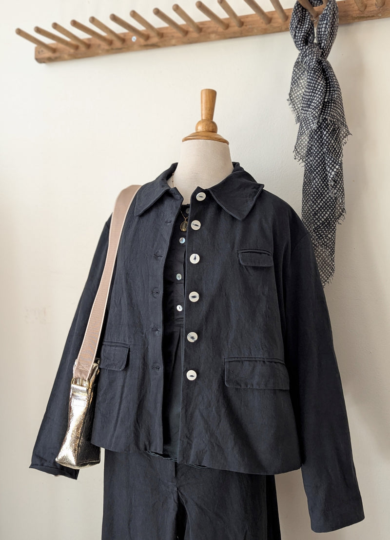 Black twill jacket and pants on a mannequin with a gold bag against a neutral background