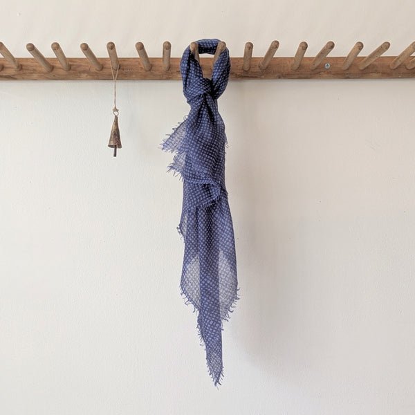 Blue patterned scarf hanging on a wooden coat rack against a white wall.