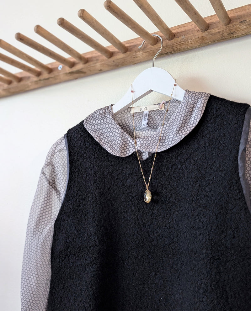 Black wool silk vest with a patterned collared shirt and necklace hanging on a wooden rack.