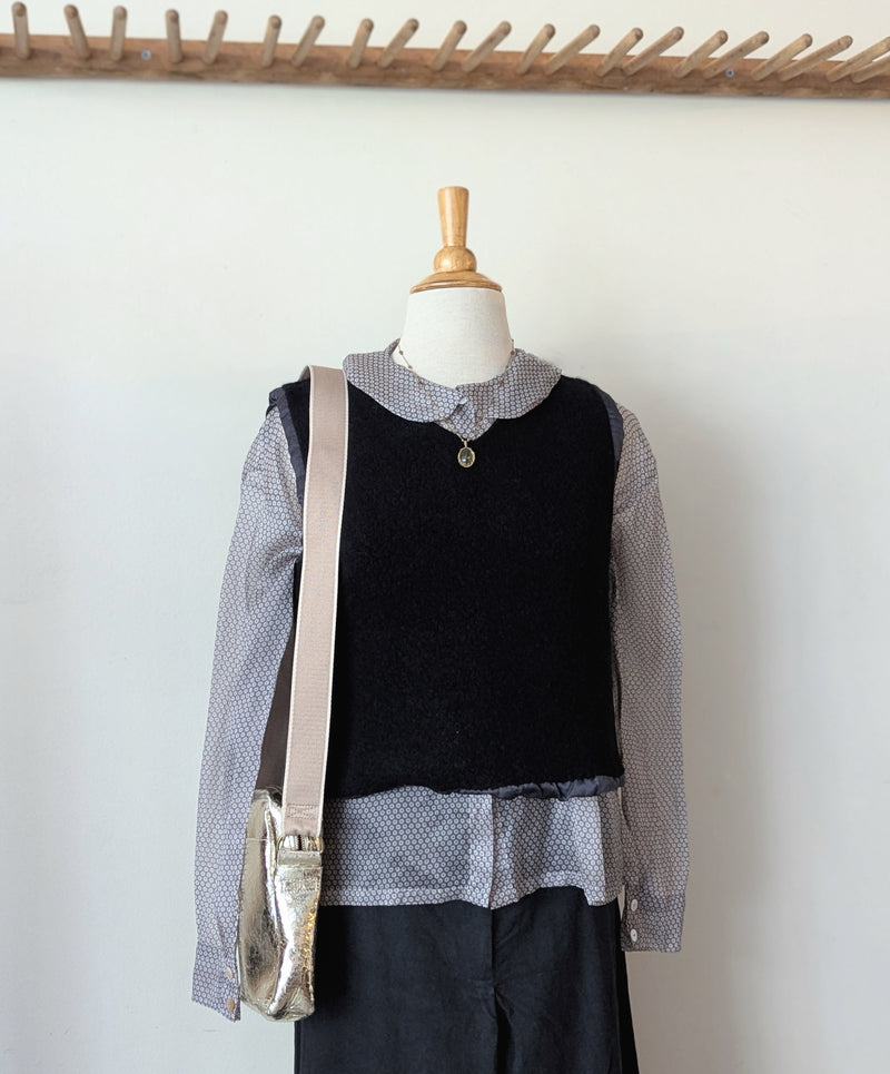 Mannequin wearing a layered outfit with a black wool vest, gray silk organza patterned shirt, and pants against a white wall.