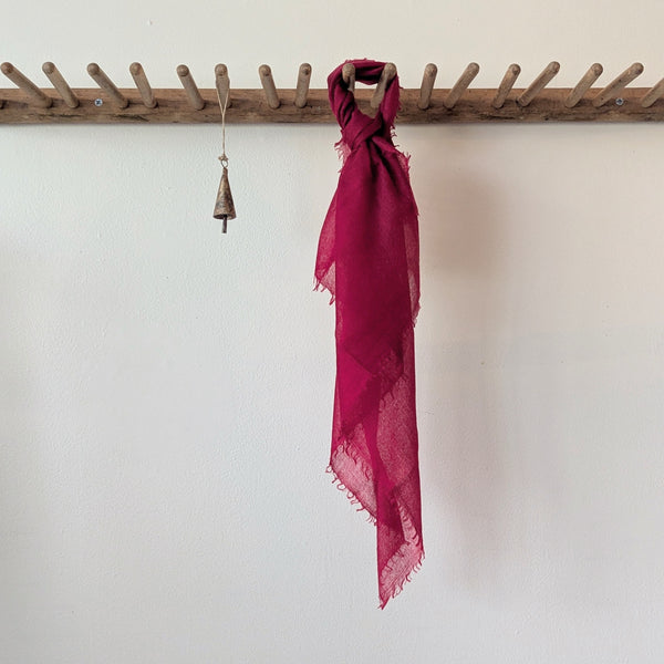 Red scarf hanging on a wooden rack against a white wall