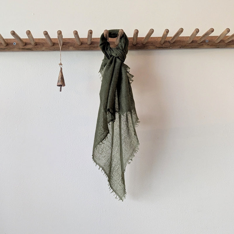 Green scarf hanging on a wooden rack against a white wall