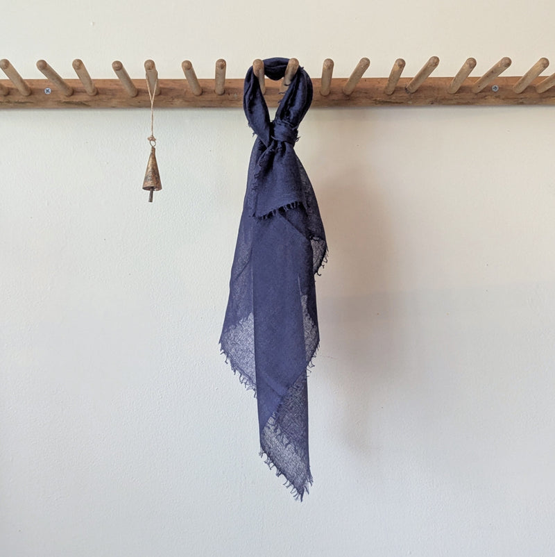Navy blue scarf draped over a wooden coat rack against a white wall.