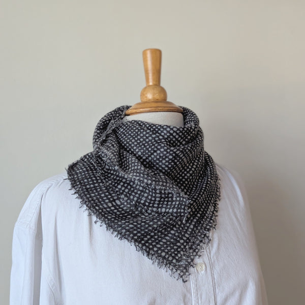 Black patterned scarf draped over a mannequin wearing a white shirt against a neutral background