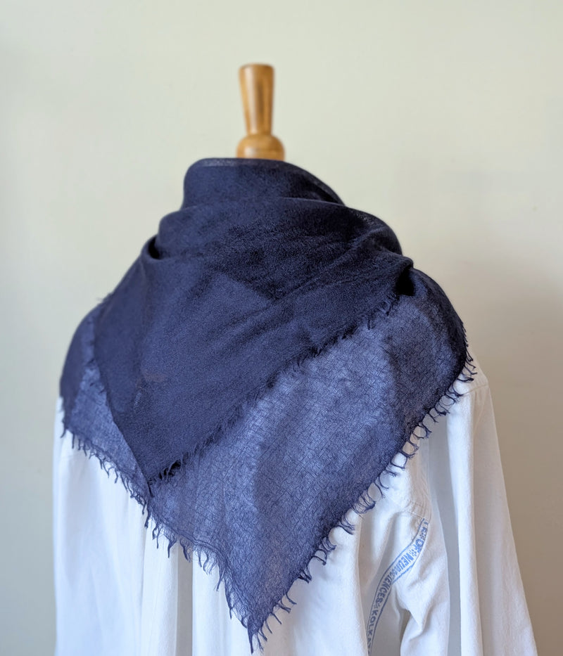 Navy blue scarf draped over a white garment on a mannequin against a plain background